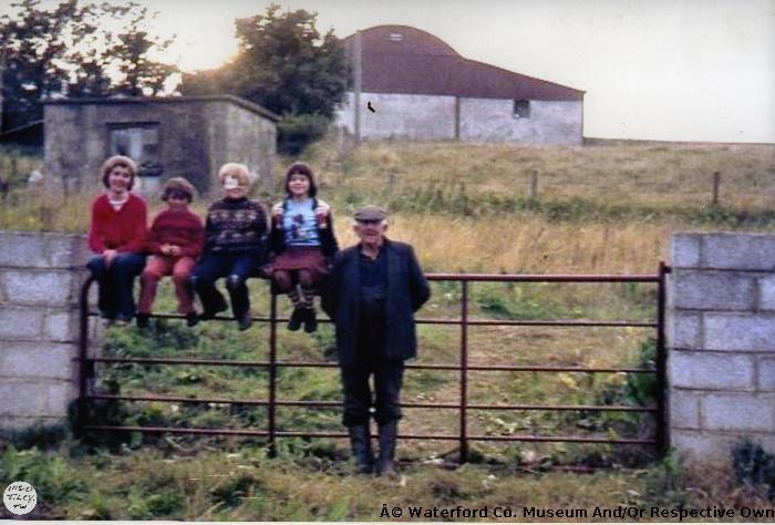 Children Sitting On Gate With Man To The Right In Baile na nGall, Ring.